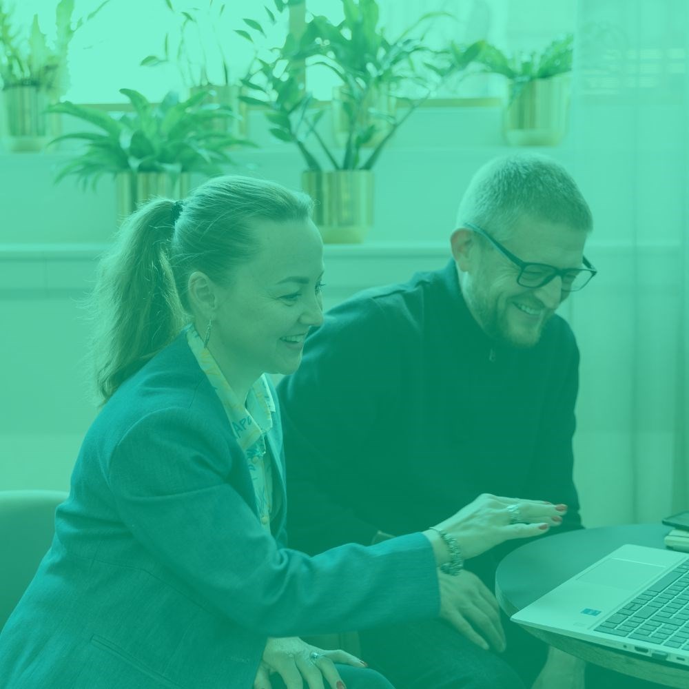Two colleagues smiling while looking at a laptop screen with a green tint 