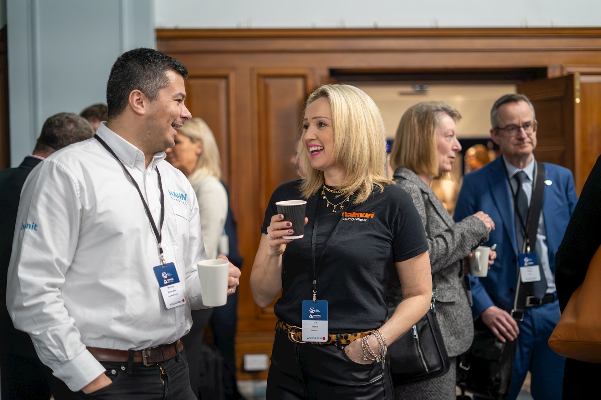 Two event attendees holding hot drinks and smiling at each other while in conversation