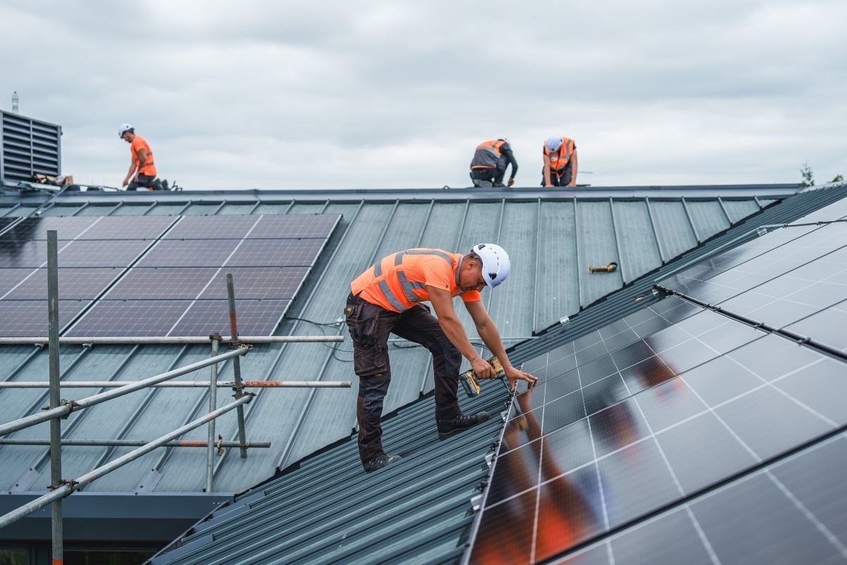 Man fitting solar panels to a roof with other workers visible in the background