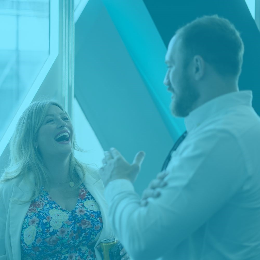 Two people laughing and smiling while having a conversation with a light blue tint